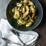 roasted brussels in a black bowl with a napkin and metal tongs