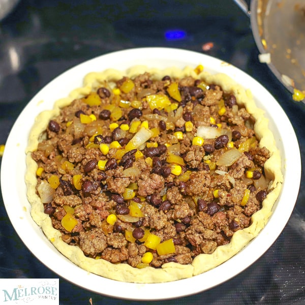 Taco pie filling - ground beef, corn, onions, peppers, beans and seasonings in a pie crust sitting on top of the oven.