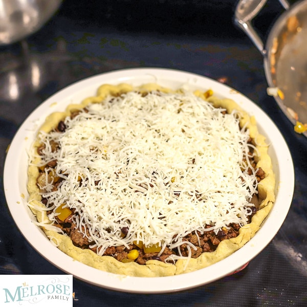 Pie shell with taco filling and covered in cheese on top of the stove.