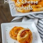 two ham and cheese pinwheels on a whilte plate with more pinwheels behind