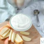 yogurt fruit dip in a teal bowl on a cutting board with apples surrounding it.