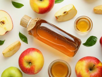 a homemade apple ciders placed in a big bottle and small glass bowls with fresh slices and whole apples on the sides