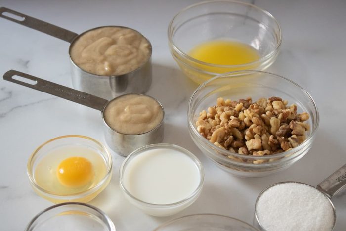 two cups of mashed banana, melted butter, egg, sugar, flour and nuts placed in a measuring cup and small bowls