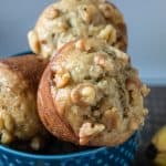 Golden banana nut muffins, looking super filling with their full, round sides, are nestled in a bowl. The crunchy nuts on top add a tasty contrast, making you yearn to pick one up for a satisfying bite.