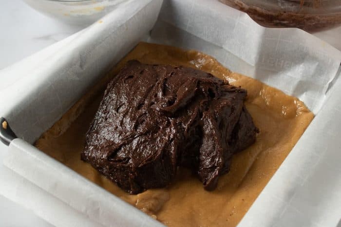 the chocolate batter mixture is poured into the peanut butter mixture on a baking tray
