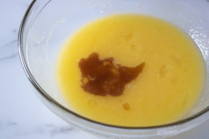 a large glass mixing bowl with mixed sugar and eggs with newly added vanilla extract ready for stirring