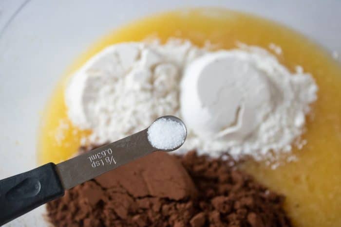 a close up image of a teaspoon full of salt while other ingredients in a large glass bowl can be seen on the background