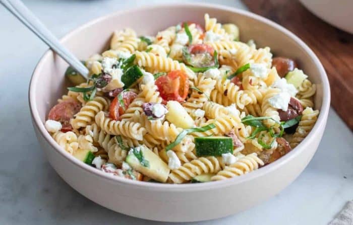 a bowl of chickpea pasta salad, brimming with fresh zucchini, cherry tomatoes, goat cheese, tangy Kalamata olives, and a shallot oregano dressing