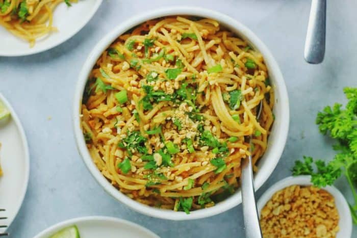 Asian-inspired pasta dish with these creamy, gluten-free peanut butter noodles topped with nuts and green herbs
