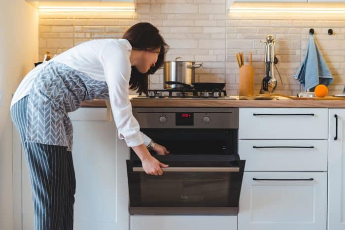a young woman wearing apron is putting the sliced figs inside the oven on her kitchen with white cabinets