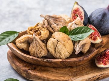 fresh and dried figs are placed in a wooden bowl with fresh leaves on top for additional color