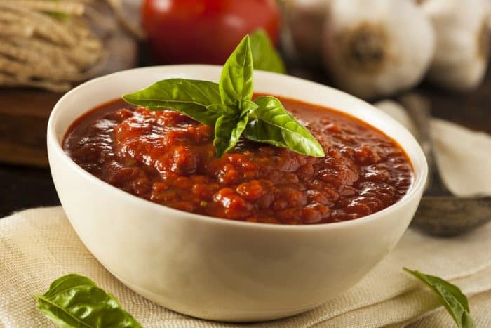a white bowl full of Homemade Red Italian Marinara Sauce with Basil and Garlic on a kitchen table