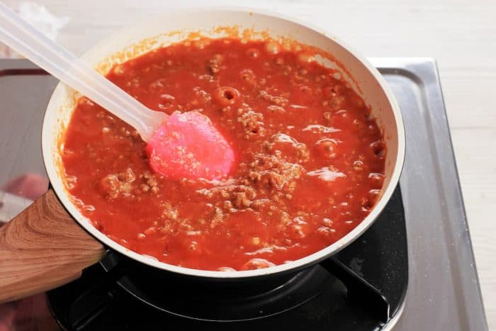 a spaghetti sauce on a pan cooking on a stove with silicon spatula for stirring