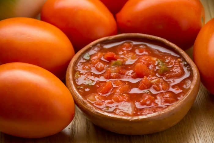 a bowl of homemade Mexican salsa with fresh tomatoes on the side