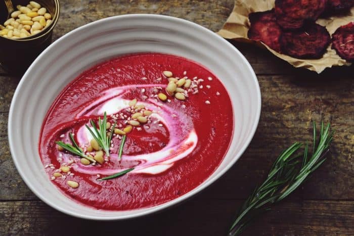 a white bowl full of carrots and beets puree soup garnished with different spices