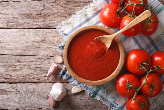 tomato sauce with garlic and basil in a wooden bowl placed on a kitchen towel at a wooden table