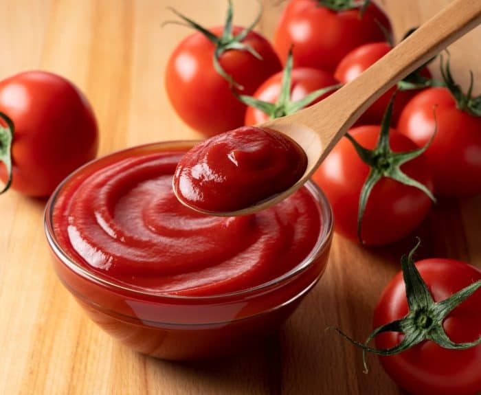 Close up of ketchup and tomatoes placed on a wooden background.