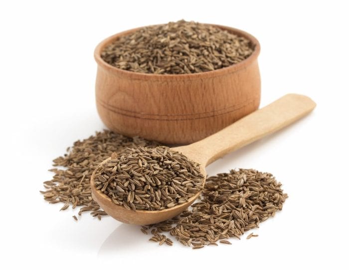 a wooden bowl and spoon full of cumin seeds isolated on a white background