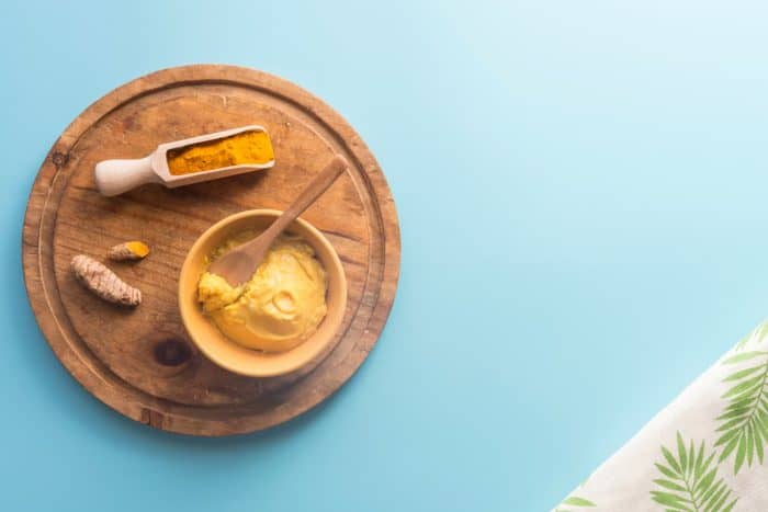 fresh, ground and paste turmeric placed in a wooden plate on a blue background