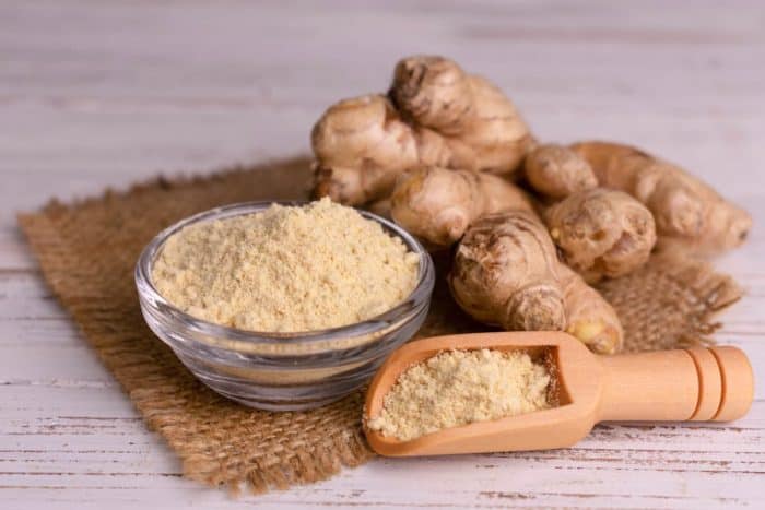Fresh dried ginger and a bowl full of ginger powder on a white wooden background.