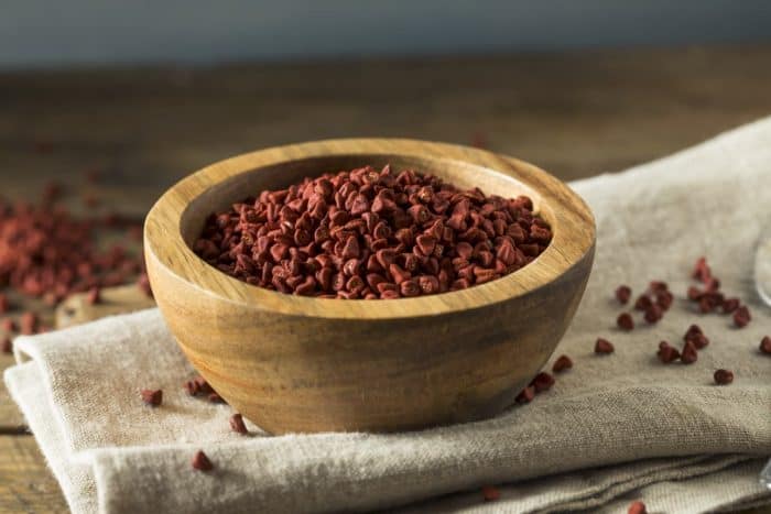 Raw Red Organic Annatto Seeds in a wooden bowl placed on a kitchen cloth