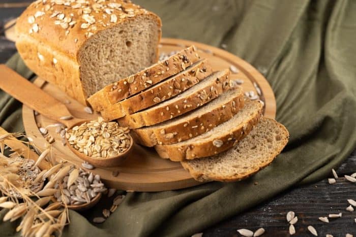 Multigrain bread on a wooden board with ears of rye and oats on a rustic cloth in the background, homemade baking concept
