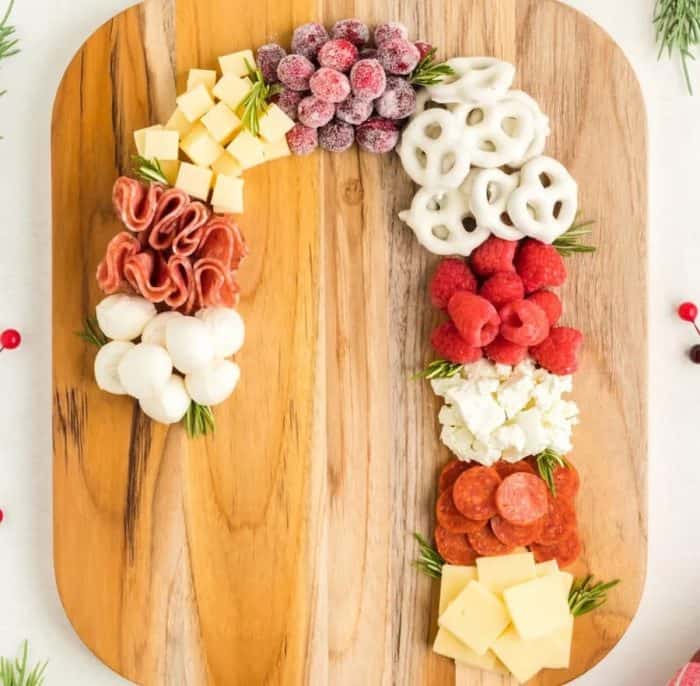 candy-shaped Christmas charcuterie board with white pretzels, sugared cranberries, fresh raspberries, sweet treats, salami, and various cheeses