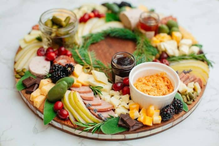 Christmas-wreath inspired charcuterie board with various cheeses, deli meats, fruits, crackers, and spreads