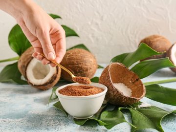 Woman holding spoon of sweet coconut sugar on color background