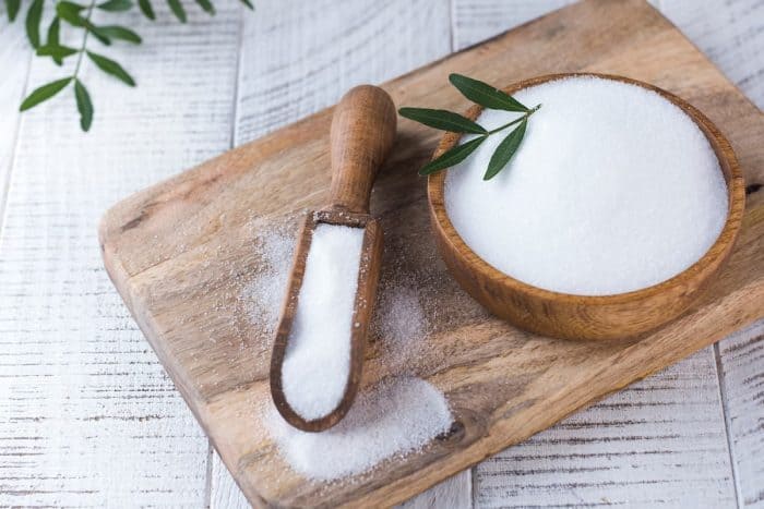 a wooden bowl and scooper full of natural sweetener placed on a wooden chopping board