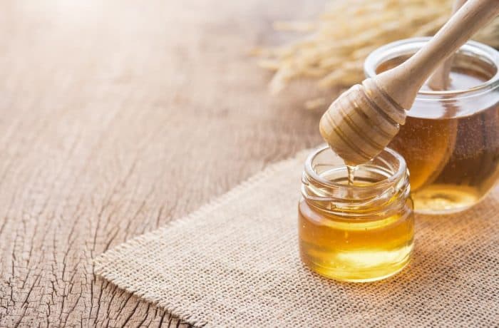 Honey with wooden honey dipper on wooden table with a mat
