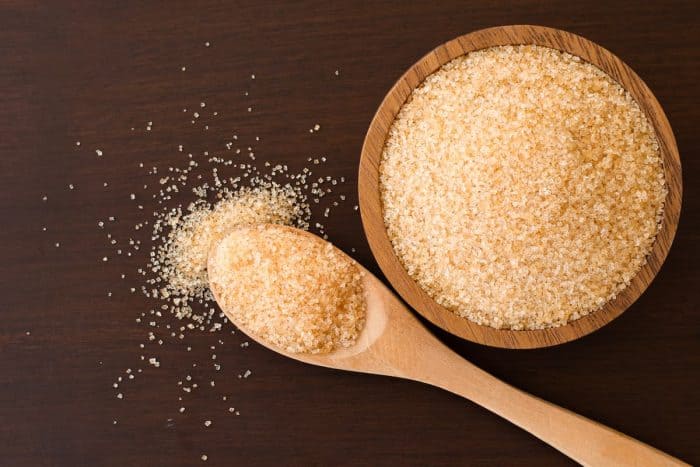 Brown sugar in wooden bowl and spoon isolated on wooden table background.