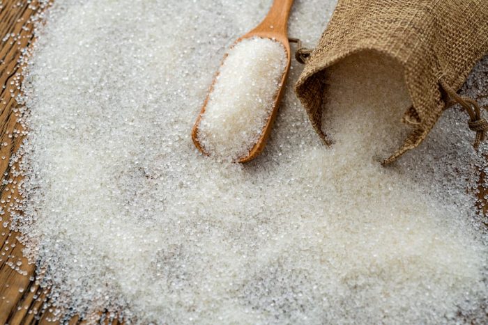 Granulated sugar in sack bag scattered on a wooden table