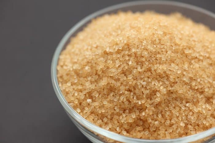 Brown cane sugar in a glass bowl on black background.