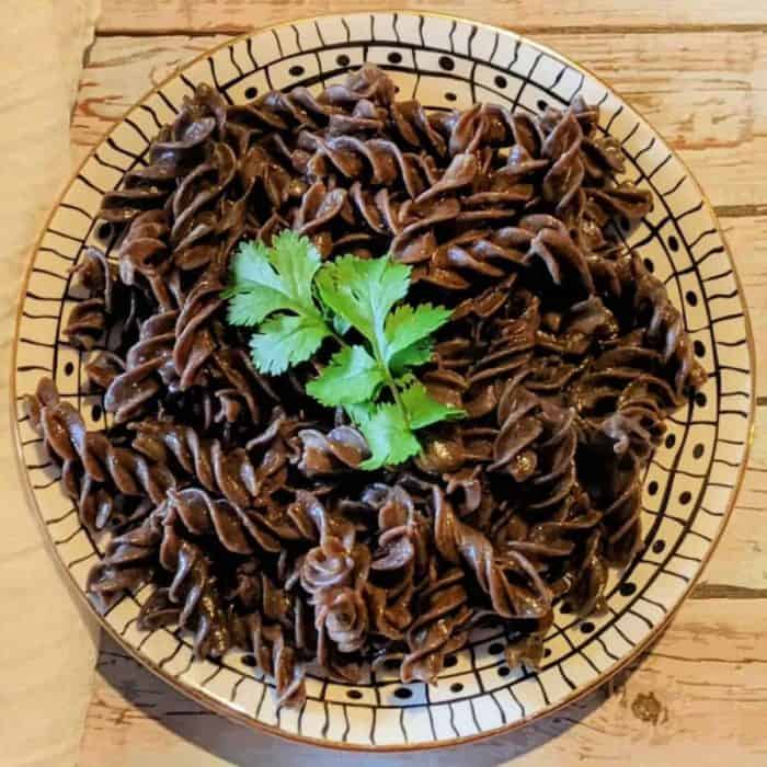 banana-based fusilli pasta is bathed in a simple sauce made of butter, lemon juice, garlic, salt, and black pepper placed in a plate with geometric design topped with a green herb