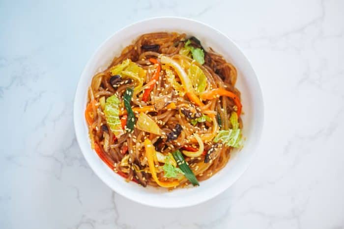 spicy vegan japchae made with a stir-fried blend of sweet potato glass noodles, vibrant vegetables, earthy shiitake mushrooms, and a fiery gochujang-based sauce