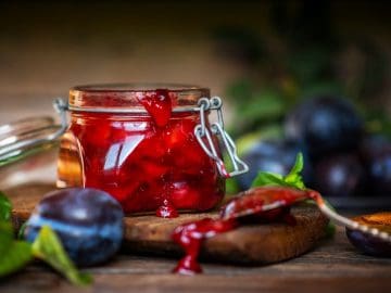 Plum sauce in a jar and blue ripe plums on a table.