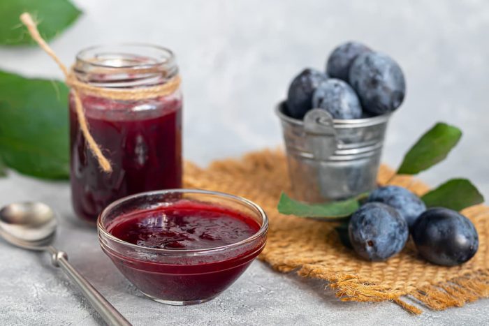 Plum jam in a jar. In the background there are plums.