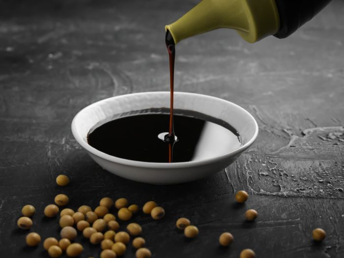 Pouring sweet soy sauce into white ceramic bowl from bottle on black background.
