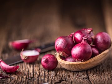 a bunch of Red onions on very old oak wooden board placed on a table