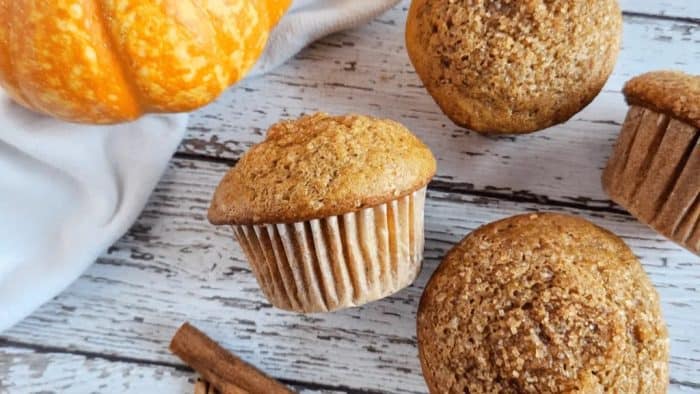 sourdough pumpkin muffins on a wooden table with real pumpkin on the sides