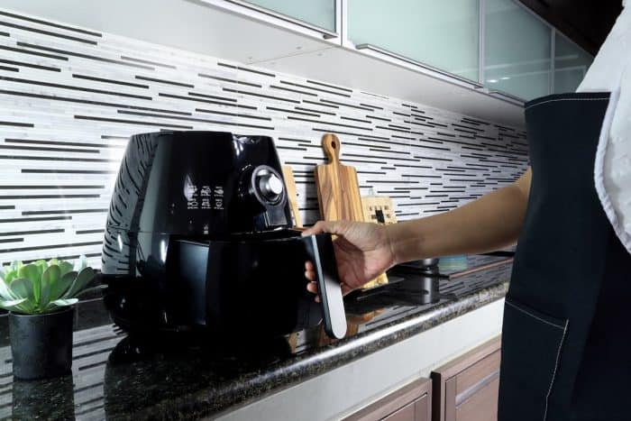 an asian lady woman is holding the tray of the air fryer or oil frying machine which is on the marble table of the modern interior design kitchen during cooking for the christmas party with her family
