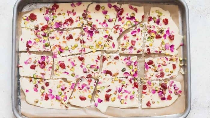 pour melted white chocolate into a sheet pan and top it with pistachios, dehydrated strawberries, and dried rose petals