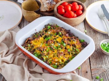 sausage and potato breakfast casserole on a wooden table with tomatoes on the side