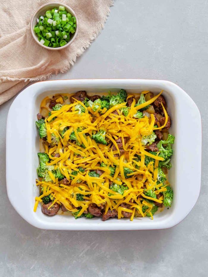 cooked sausage, potatoes, broccoli, and cheese and egg mixture assembled in a baking dish
