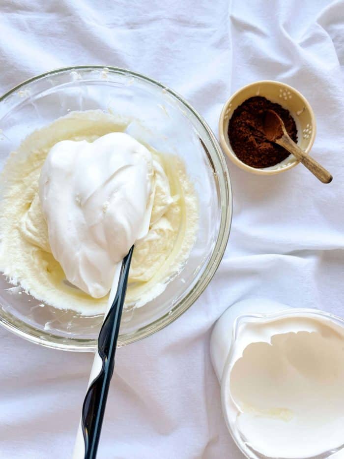 a whipped heavy cream in a bowl being slowly fold in with a spatula