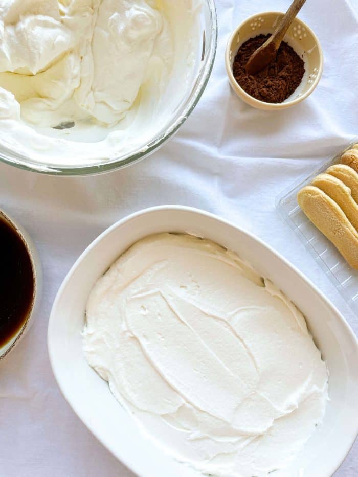a process of mascarpone cream being layered on in a casserole