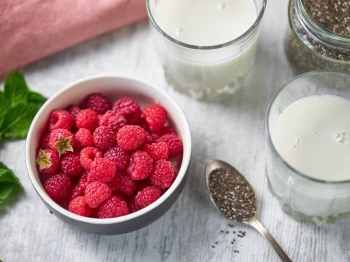 a small bowl of fresh berries, a teaspoon of chia seeds, and a cup if plant-based milk on a table