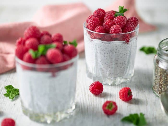 a close up photo of two cups of overnight keto chia pudding with fresh berries and mint on top