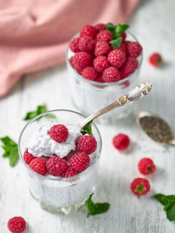 a cup of keto chia pudding with a spoon on top and fresh berries as topping